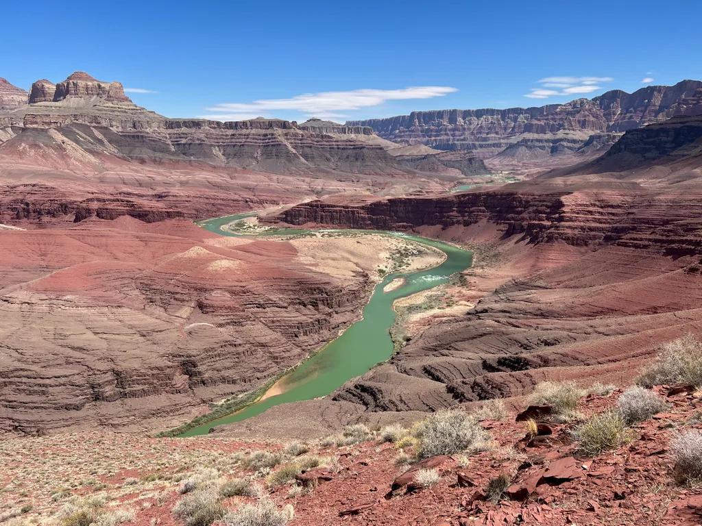 Jade-green river curving through a wide canyon of red terraced rock, with dry brush in the foreground