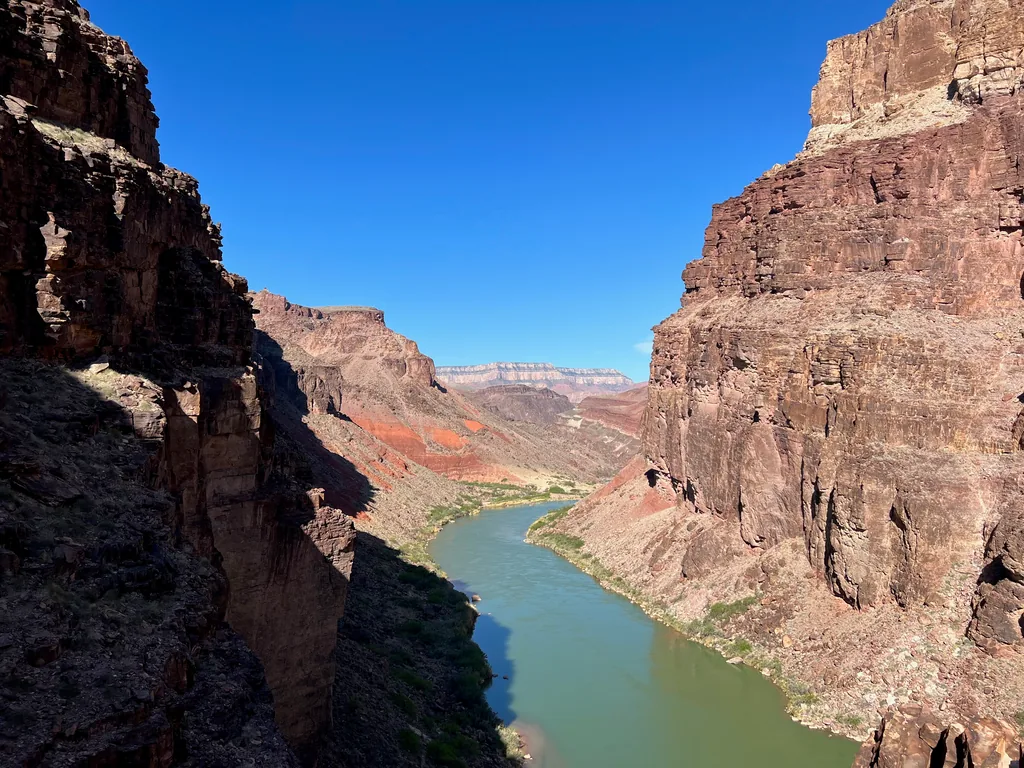 Pale green river winding between dark rock walls, with red and white cliff layers beyond under clear blue sky