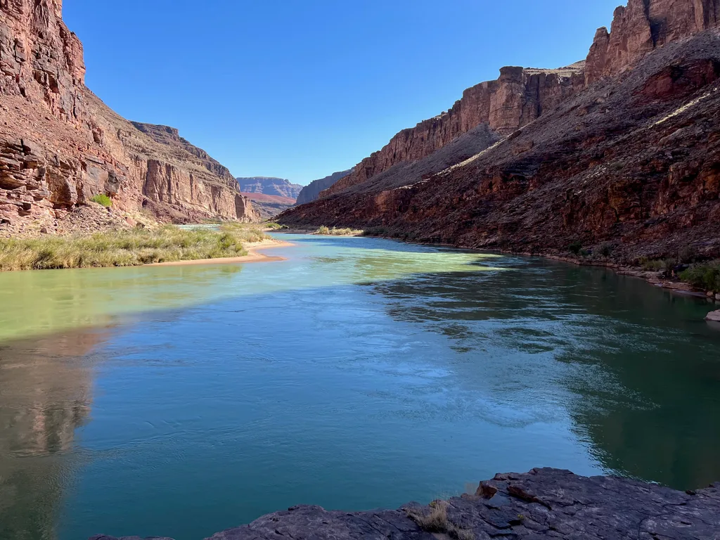 Turquoise-green river curving between red canyon walls, with a pale sandbar and grass along the left bank