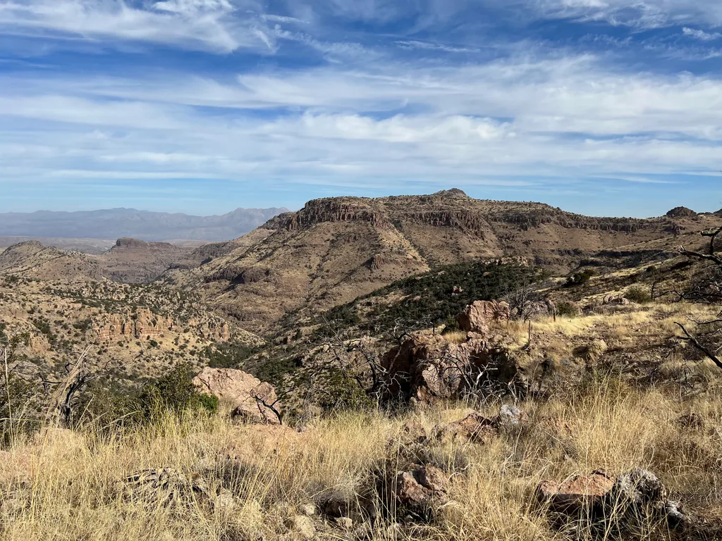 Ridge capped with a horizontal rock band across a canyon, pink boulders and dry grass in front