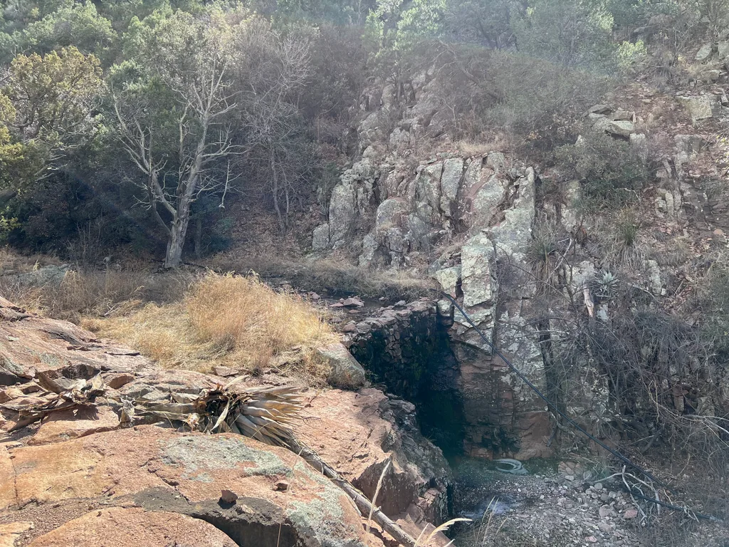 Low stone wall spanning a rock cleft above a shallow pool, with an old tire in the water below