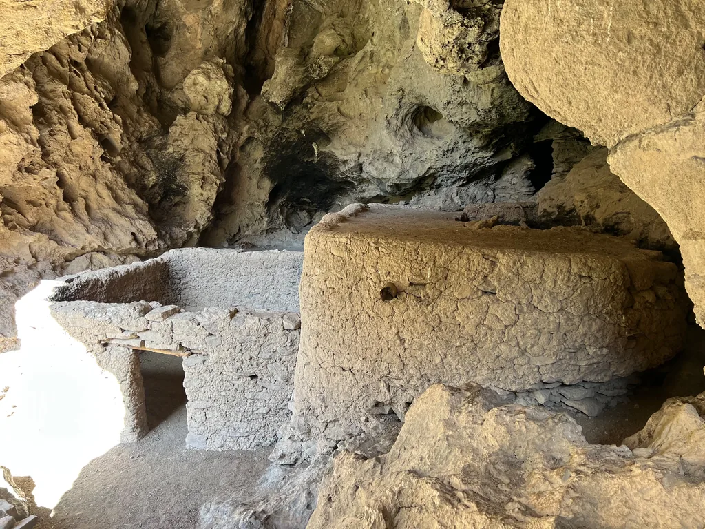 Stone and mud masonry walls with a low doorway and wood lintel built inside a rock alcove