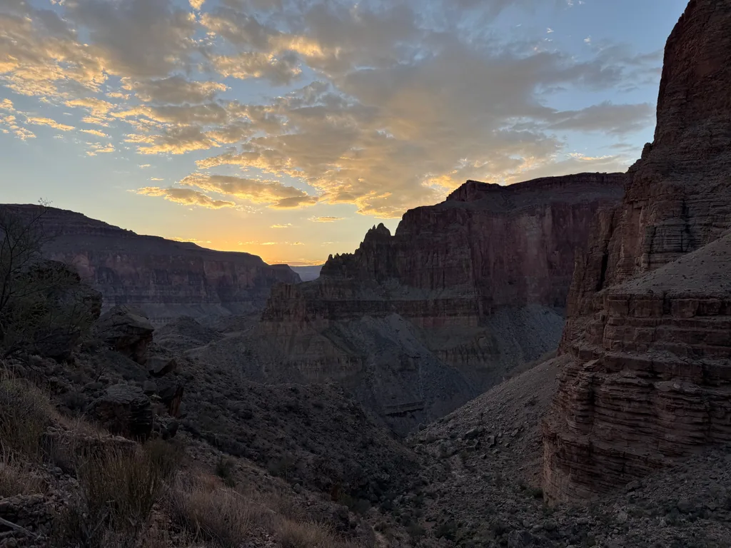 Layered red cliffs in shadow flanking a deep drainage, orange-lit clouds over the far rim